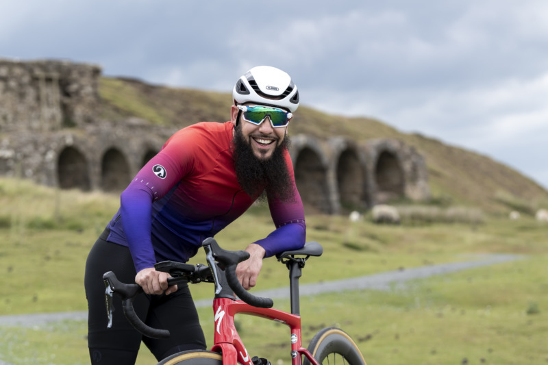 man wearing gradient red to purple design argyle ibex jersey, leaning on his handlebars and laughing 