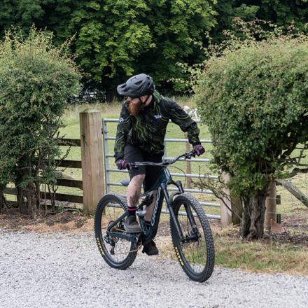 Man riding a mountain bike on a gravel track wearing the MTB Enduro jacket