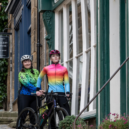 Two cyclists in women's Kiko kit standing outside a shop with their bikes