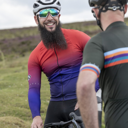 Man wearing Argyle jersey talking to another cyclist in men's Groove jersey, laughing