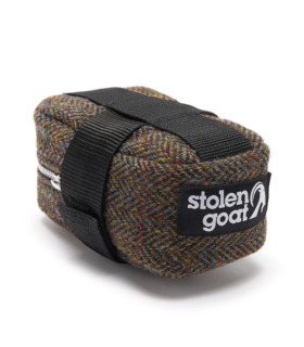 Side view of Harris Tweed saddlebag, brown herringbone fabric with black velcro attachment strap, black and white stolen goat logo label and silver metal zip