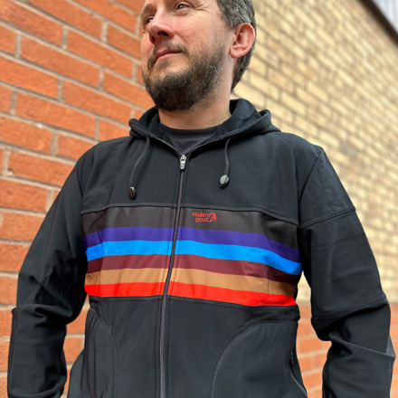 Man wearing Manta Kiko hoodie, black hoodie with red, gold, burgundy and blue block stripe across the centre of the chest.