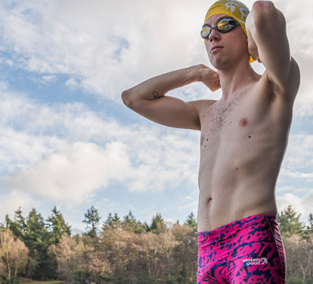 man wearing upstart jammers adjusting his swim cap next to a lake