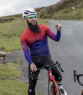 male cyclist wearing argyle red to purple fade long sleeved cycling jersey, pointing to his left and laughing