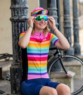 Woman sitting down putting cycling glasses on while wearing the pink stripe Arcadia jersey