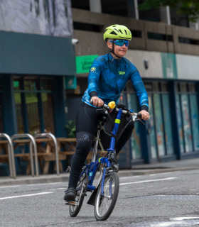 Woman riding a blue Brompton bike on a street in Bristol wearing the Wutang jersey